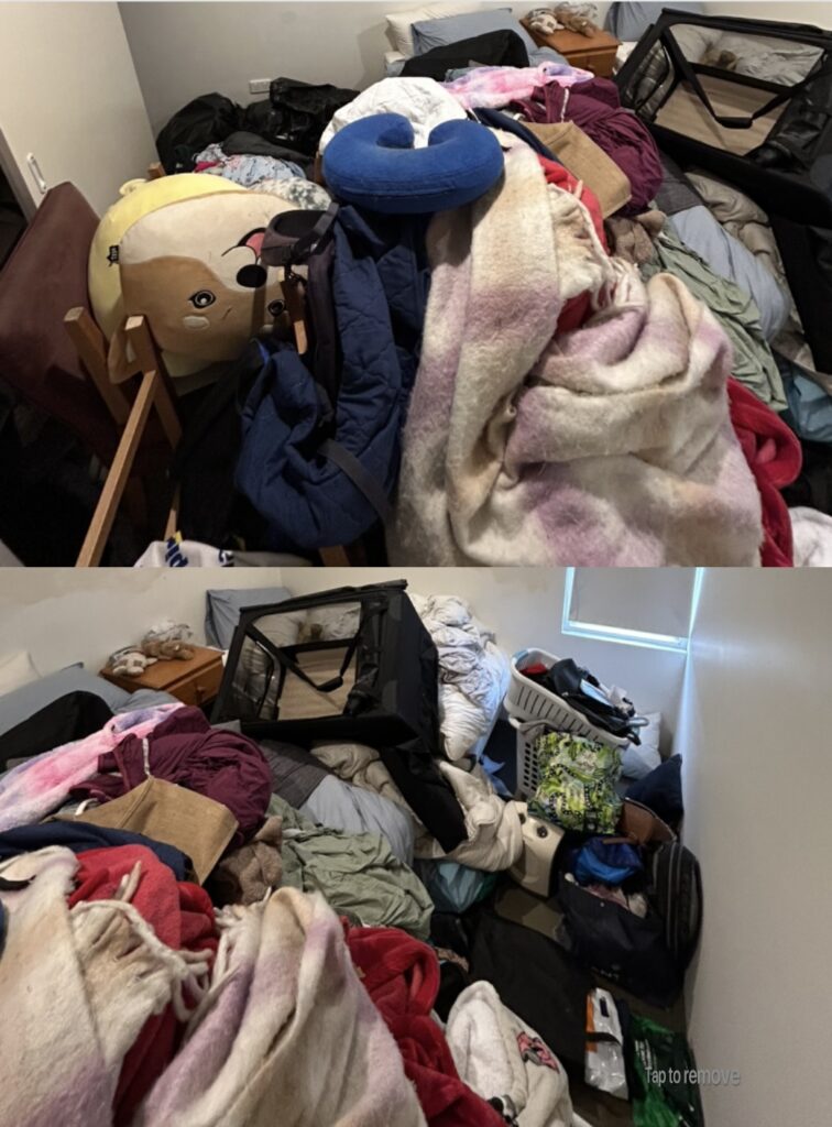 Messy bedroom with overflowing blankets, clothes, a blue neck pillow, and a portable playpen.