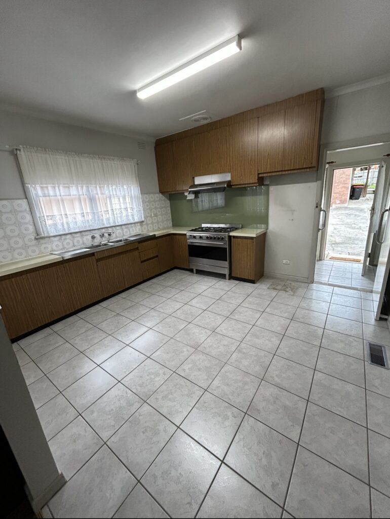 Kitchen with wooden cabinets, gas stove, stainless sink, and a pale green glass backsplash; door to outside.