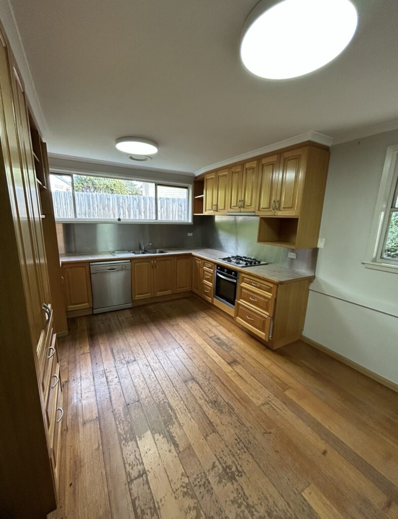 U-shaped kitchen with oak cabinets, stainless dishwasher and gas stove, and a long window overlooking a wooden fence.