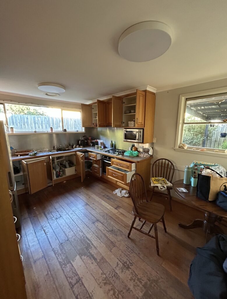 Messy kitchen with open cabinets, cluttered countertops, and a wooden dining table with chairs.