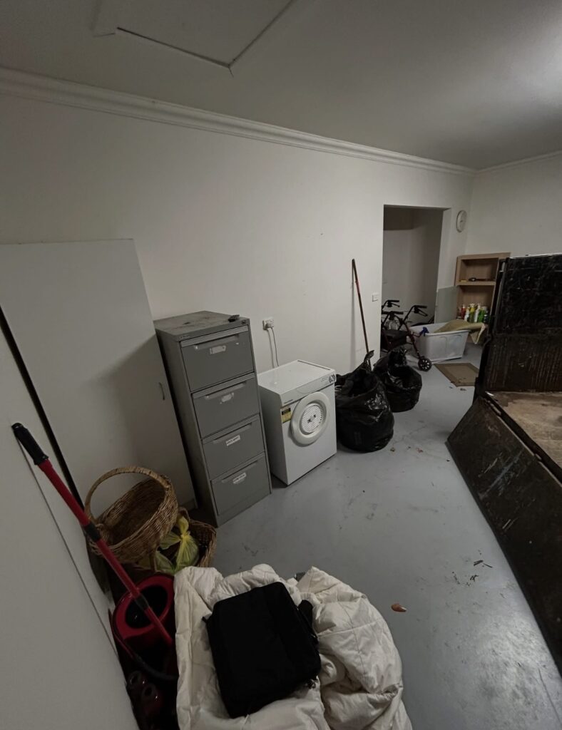 Cluttered basement storage area with a filing cabinet, washing machine, mop, baskets and bags.