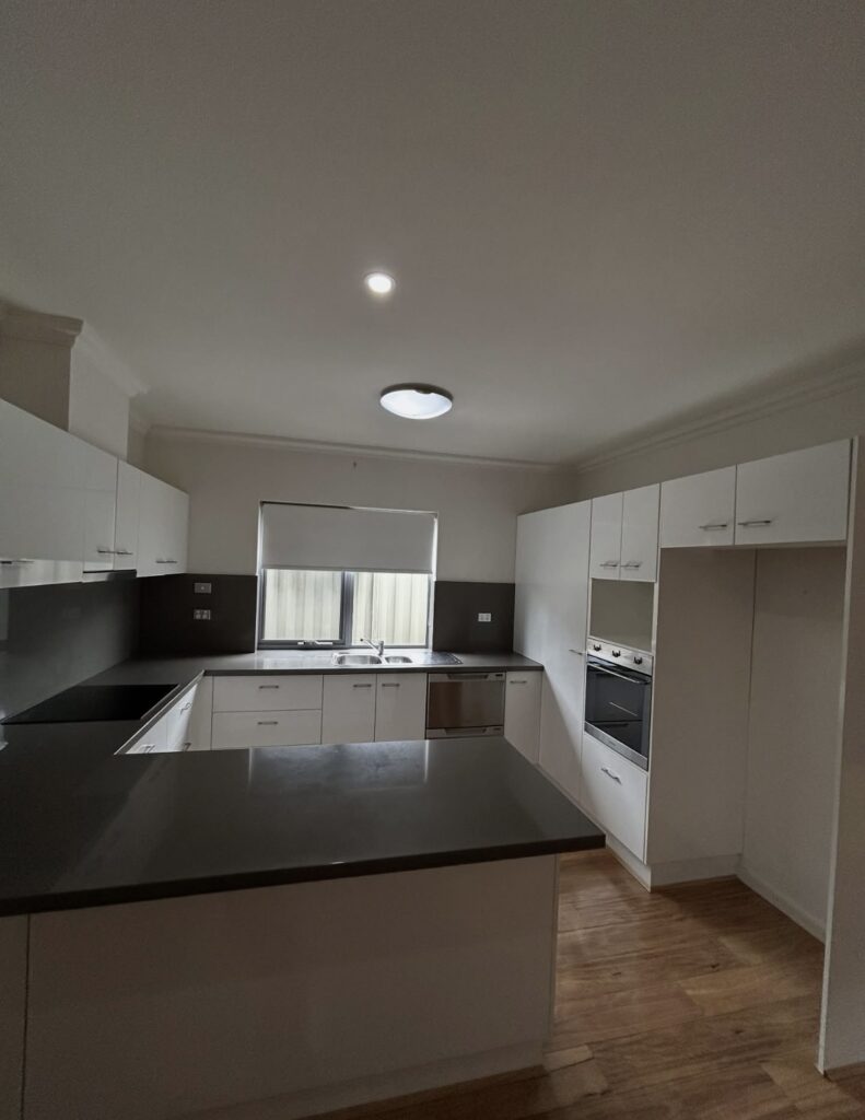 Modern white kitchen with dark countertops, island, and window above the sink.