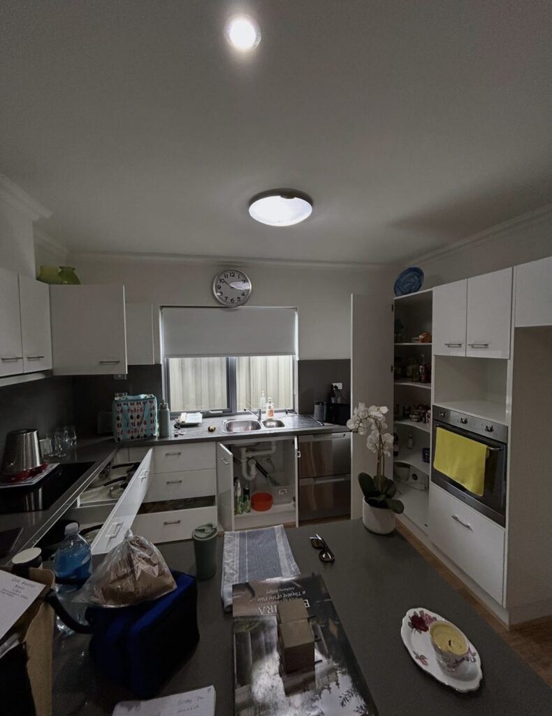 Modern white kitchen with open cabinet, sink under window, and a wall clock above the window sill.